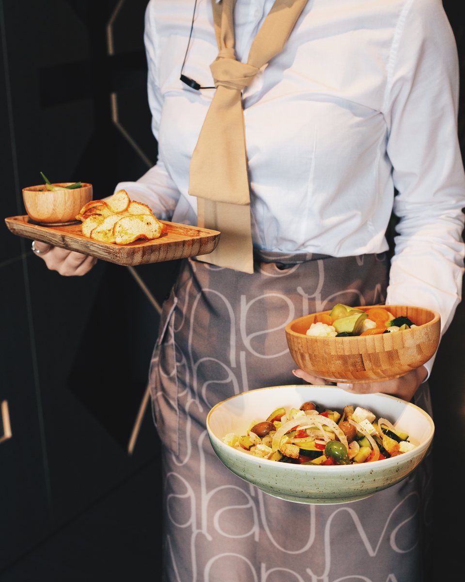 Server in an Ujvara pattern apron carrying salads and bruschetta