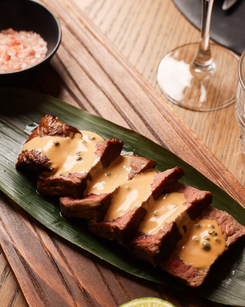 Sliced steak with green pepper sauce on a wooden board