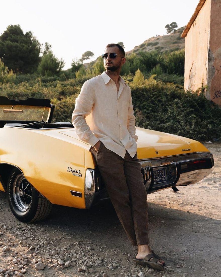 Man in a TIERR linen shirt leaning on a yellow Buick convertible