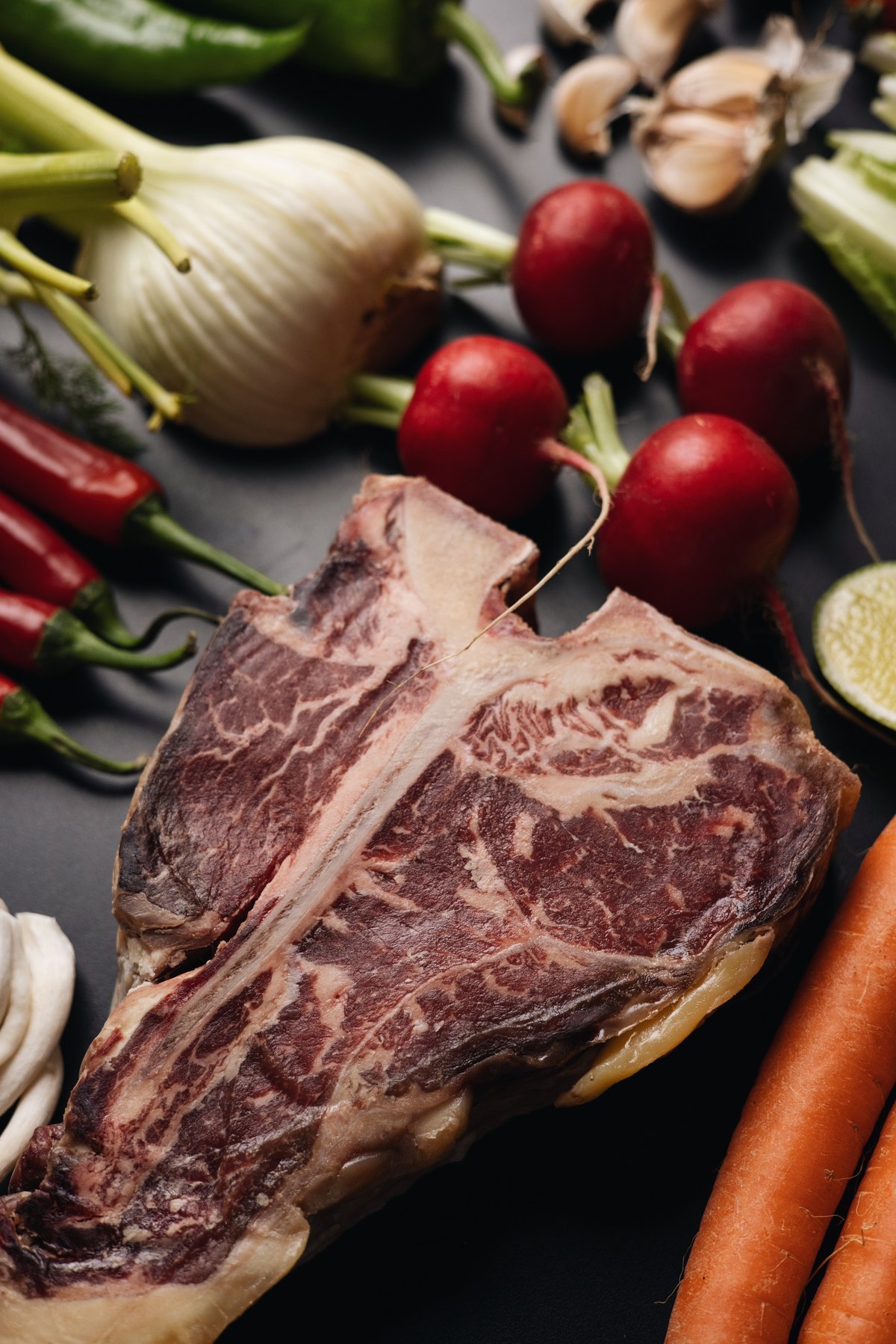Raw T-bone steak among radishes, fennel and chillies