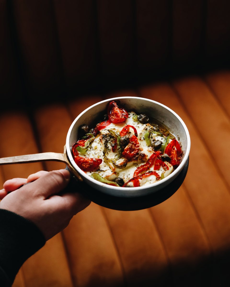 Baked cheese with peppers, tomatoes and capers in a copper pan