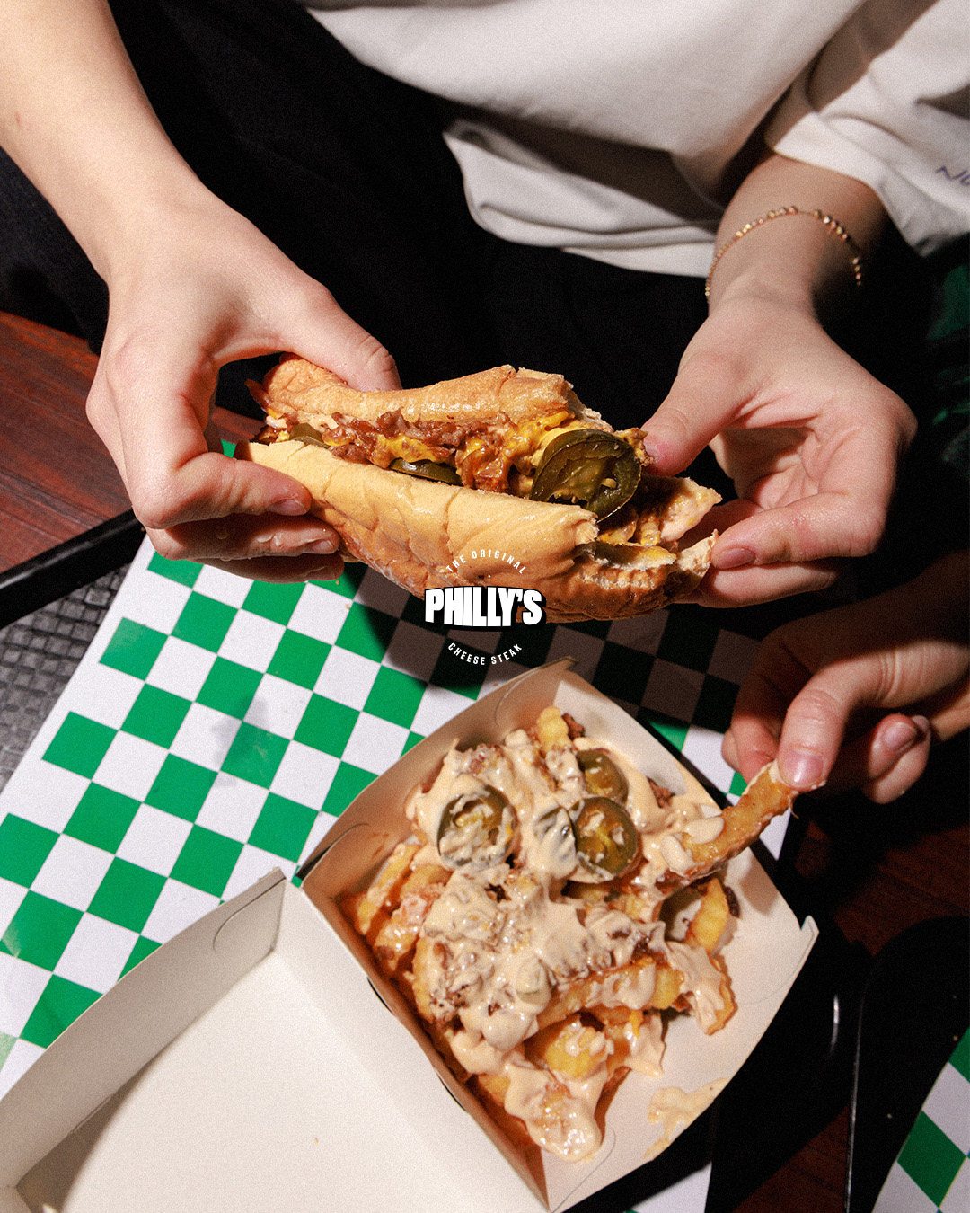Hands pulling apart a cheesesteak over loaded fries