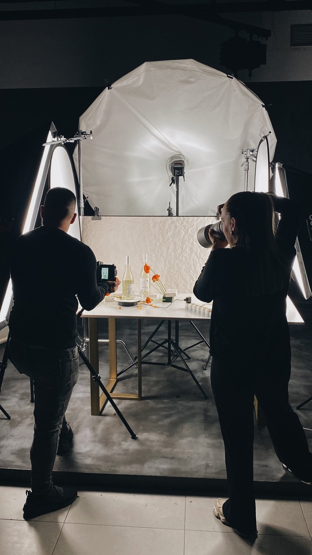 Two photographers shooting a wine still life under an octabox