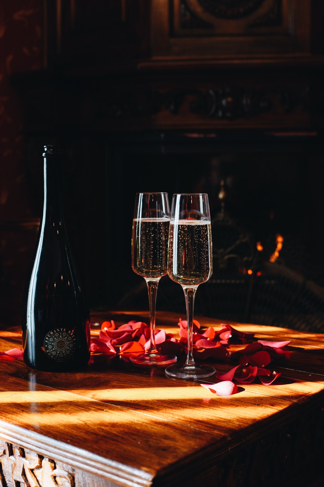 Two glasses of sparkling wine among rose petals by the fireplace