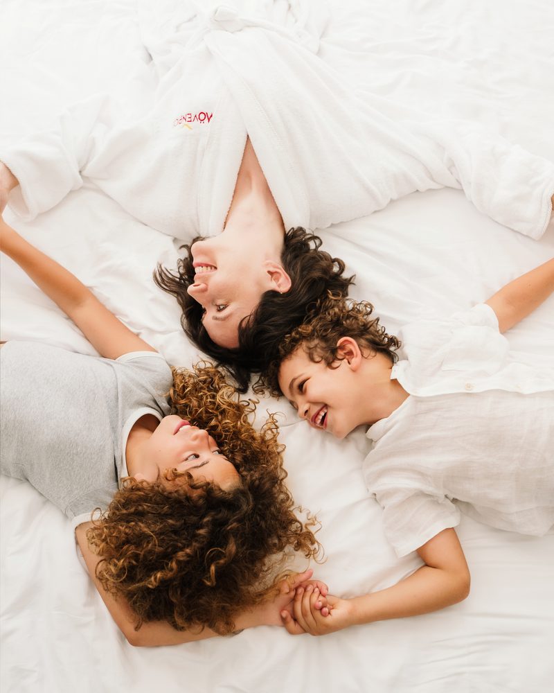 Mother and children laughing on a white bed, Mövenpick robe
