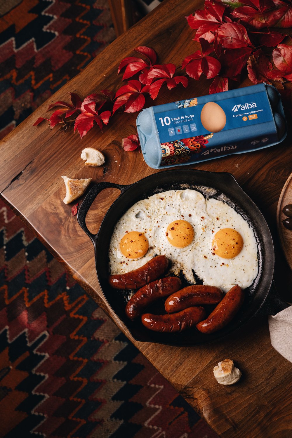 Fried eggs and sausages in a cast iron pan beside an AIBA ten-egg carton