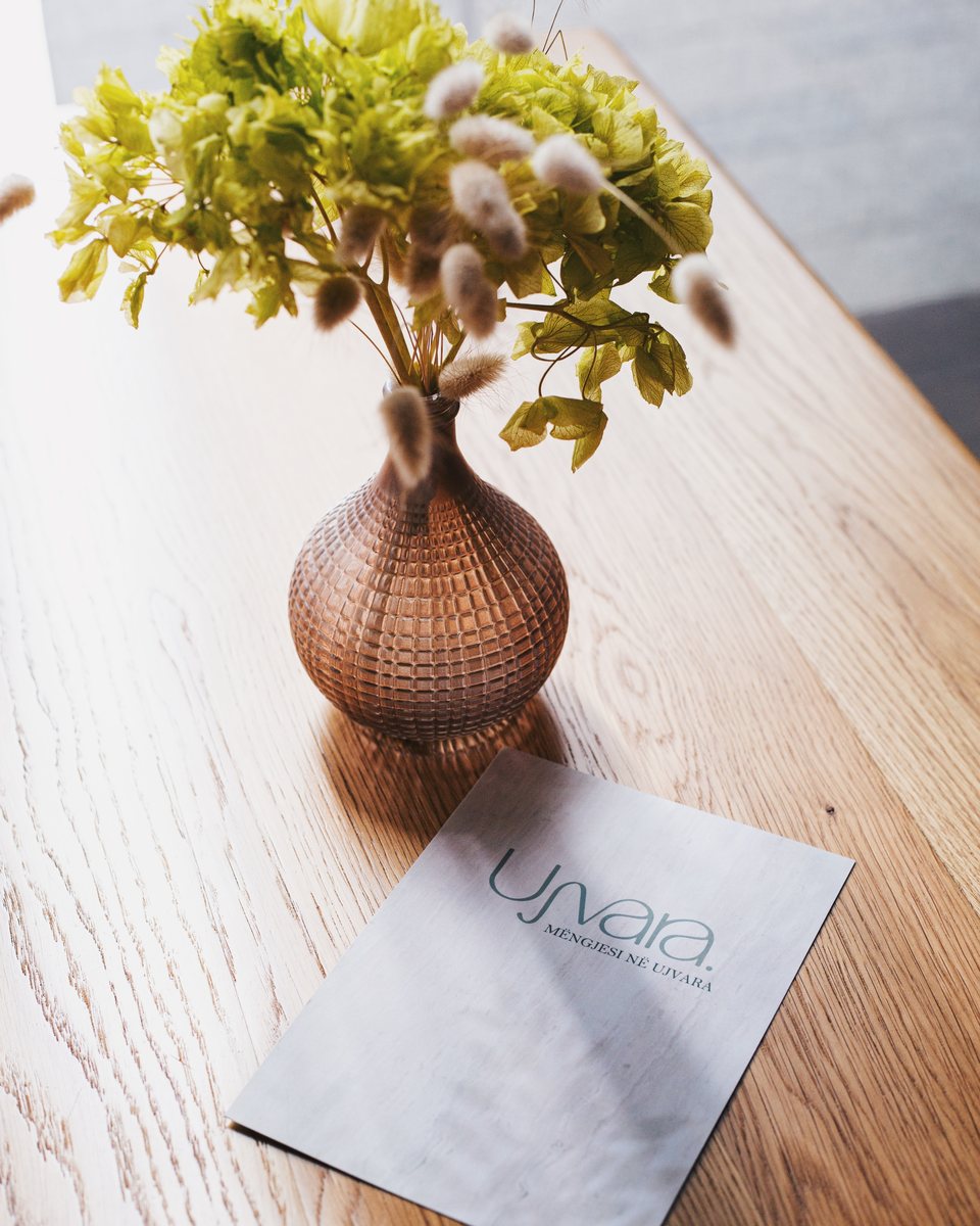 Dried flowers and the &ldquo;Mëngjesi në Ujvara&rdquo; breakfast menu on an oak table