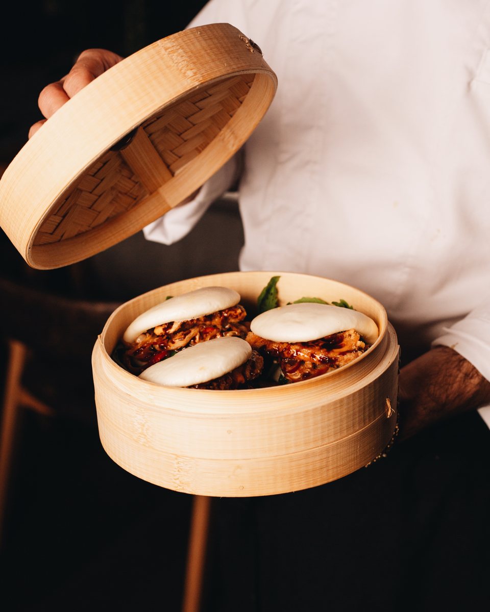 Chef opening a bamboo steamer of bao buns