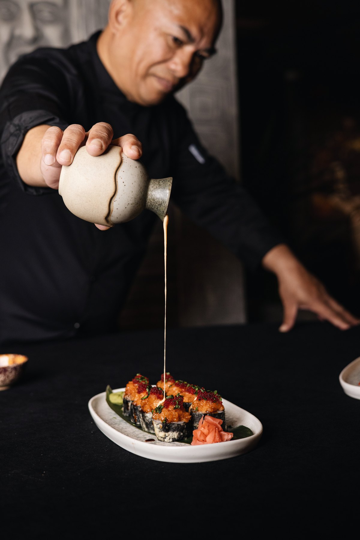 Mayfair chef pouring sauce over a plate of tempura sushi rolls