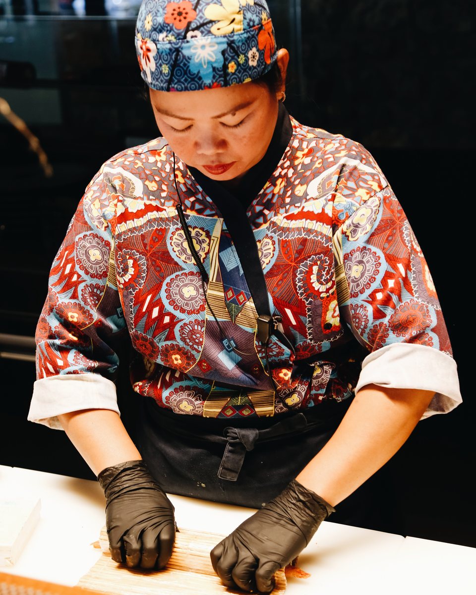 Sushi chef rolling maki in a patterned jacket