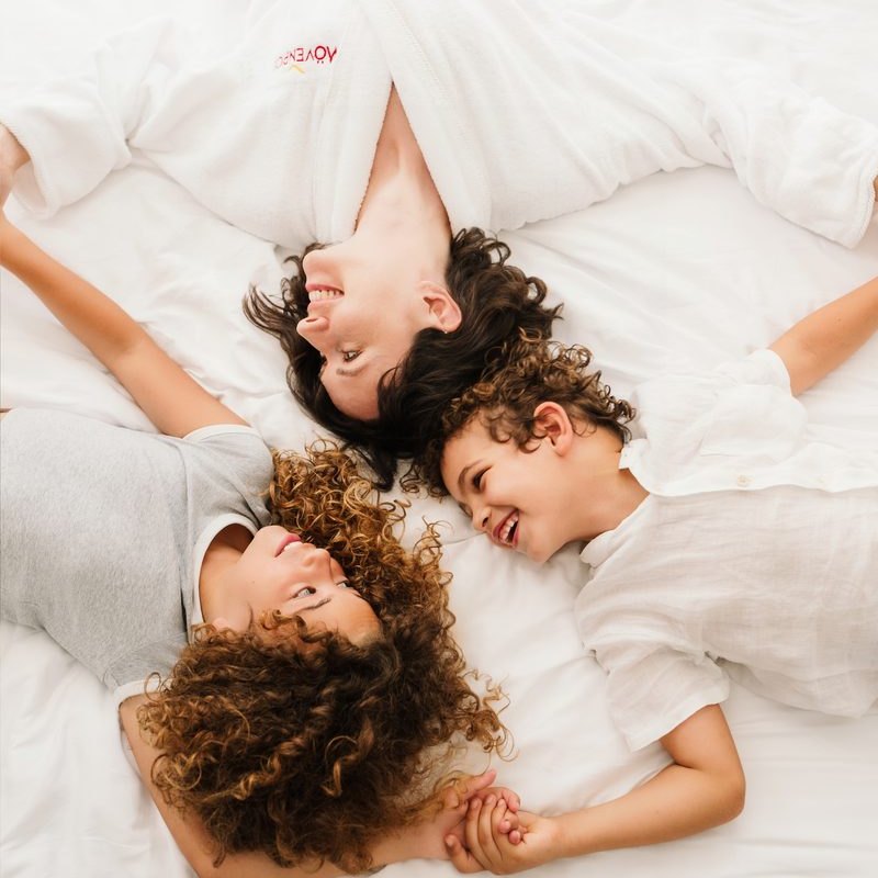 Mother and children laughing on a white bed in a Mövenpick robe