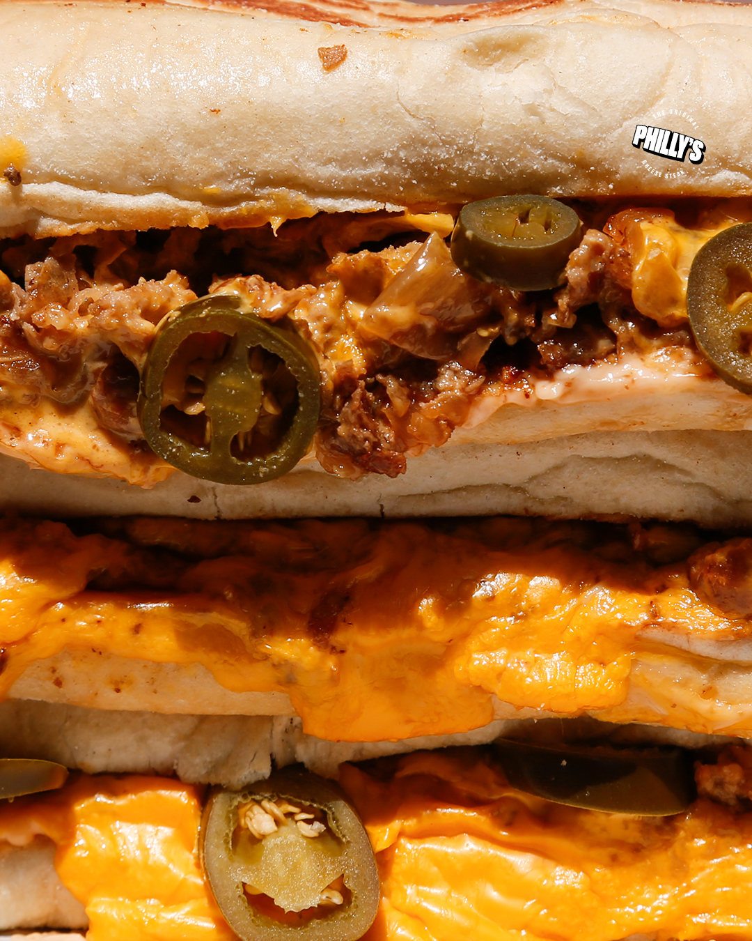 Close-up of stacked cheesesteaks with cheese and jalapeños