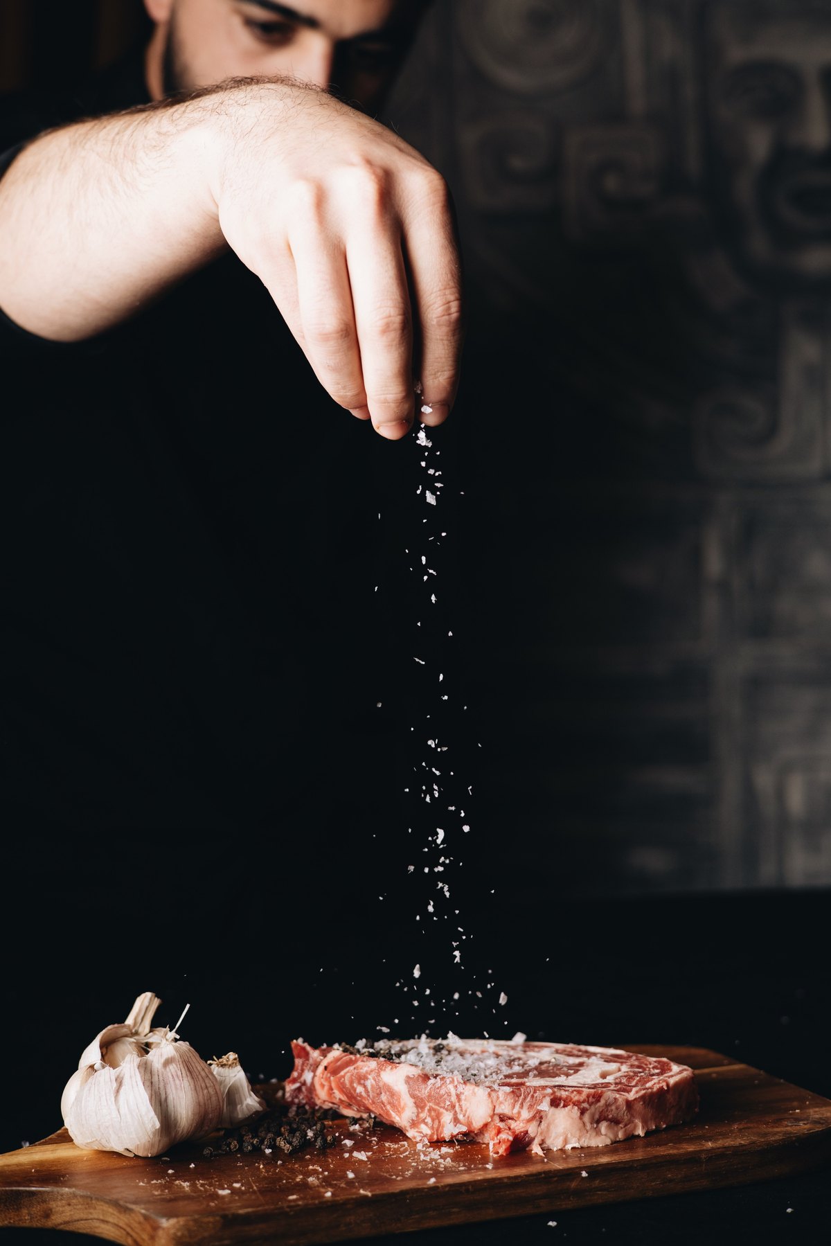 Chef sprinkling flaky salt over a raw ribeye