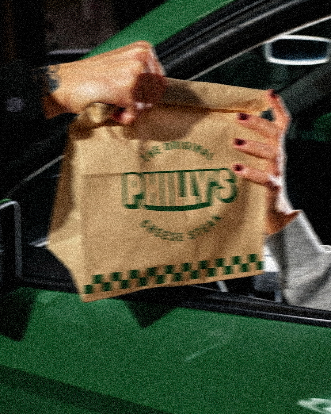 Philly&rsquo;s takeaway bag handed through a green car window