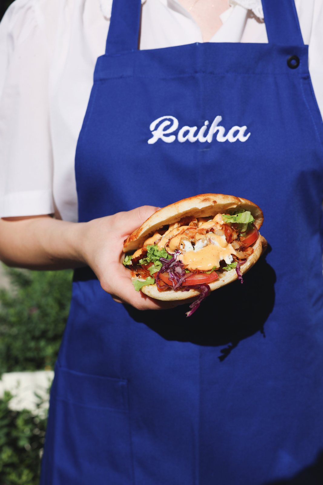 Pita kebab held in front of a blue Raiha apron