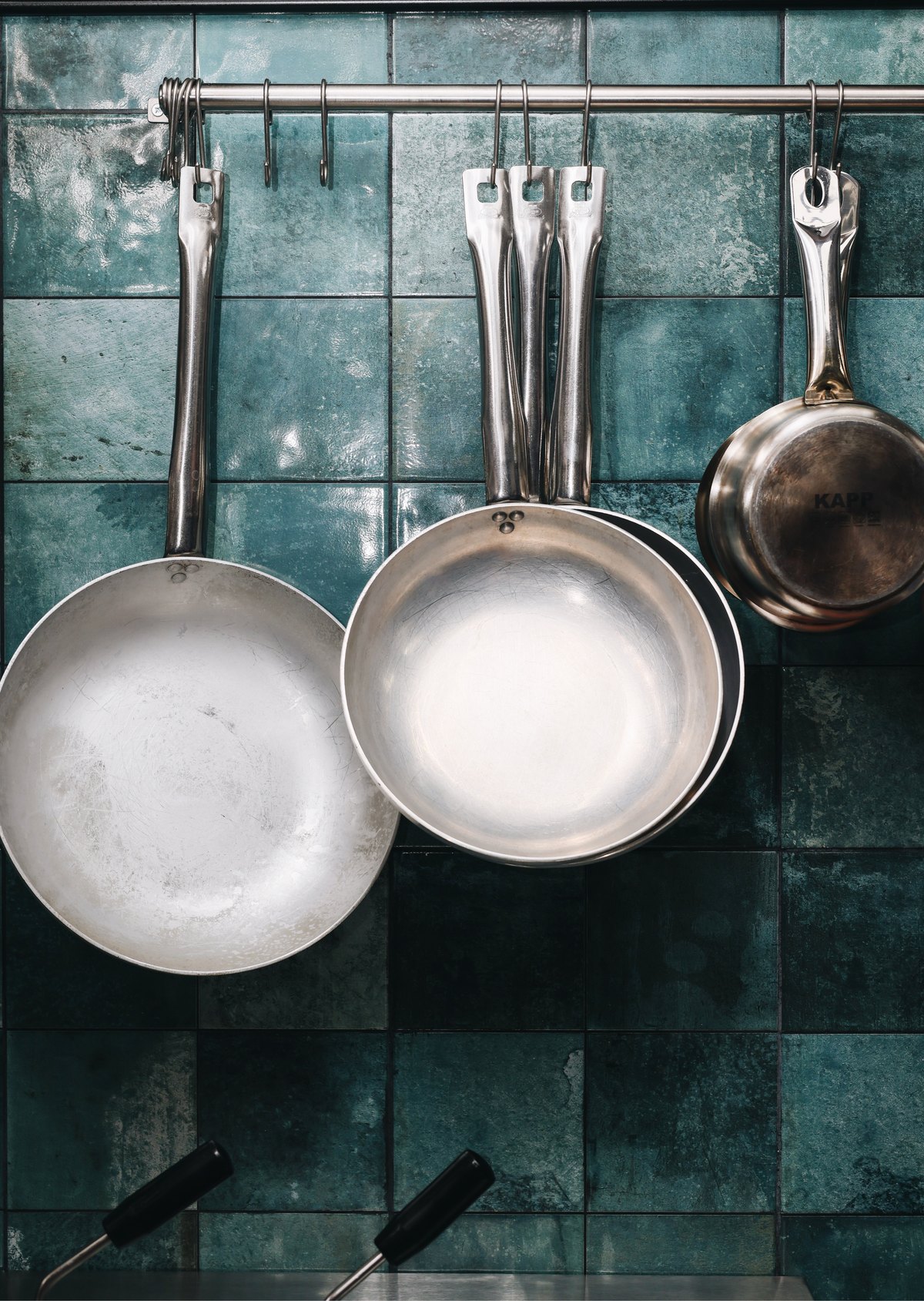 Pans hanging against teal kitchen tiles