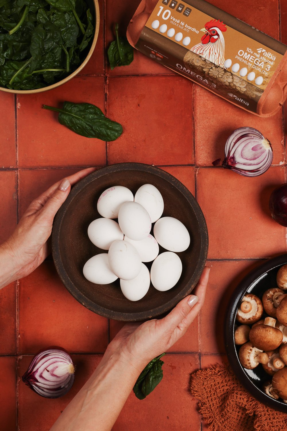 Hands holding a bowl of white AIBA eggs on a terracotta table