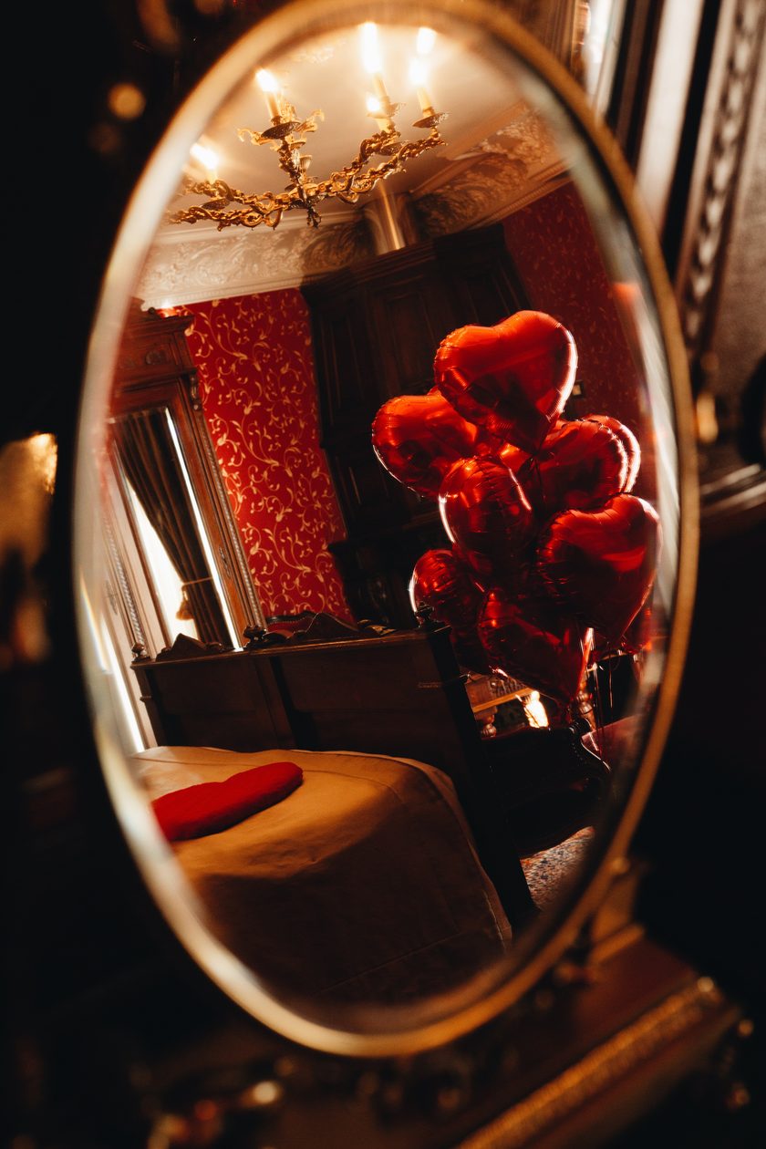 Heart balloons and a candlelit chandelier reflected in an antique mirror