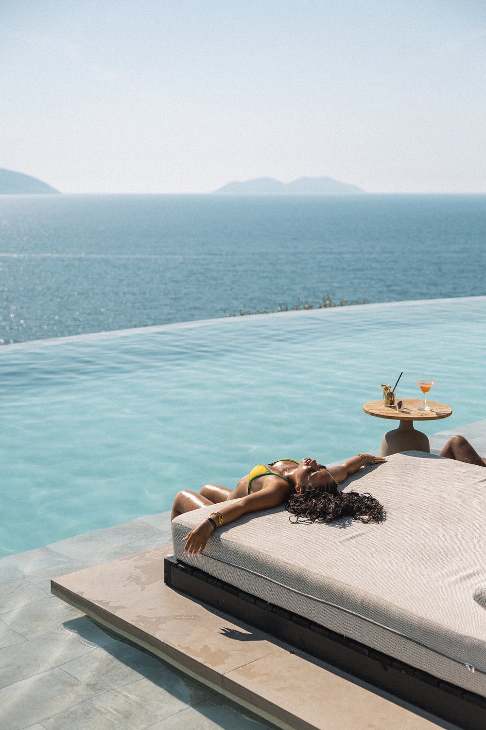 Guest sunbathing on a daybed by the infinity pool, cocktails on the side table