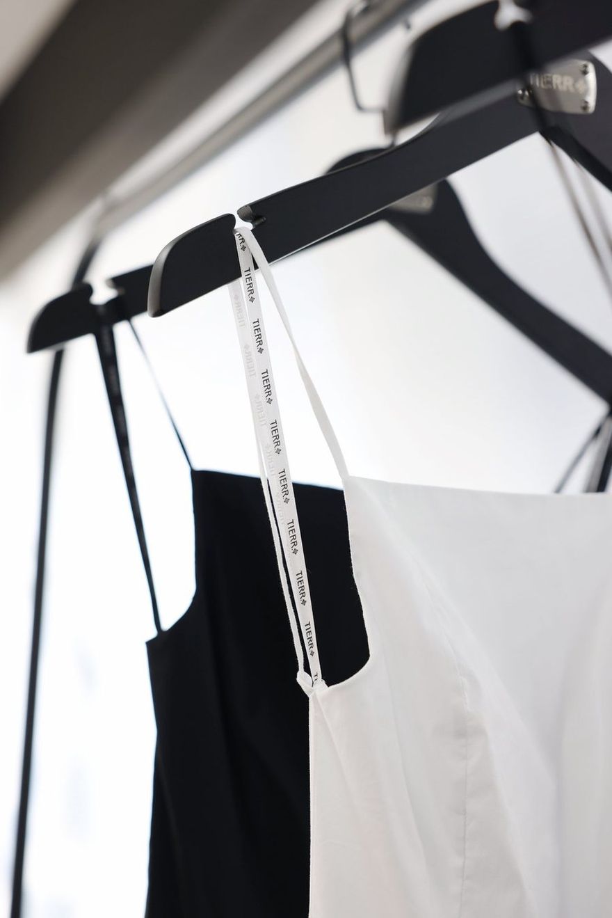 White and black TIERR slip dresses on branded hangers with a woven logo ribbon