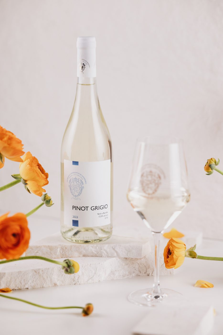 Pinot Grigio bottle and glass with orange ranunculus on stone