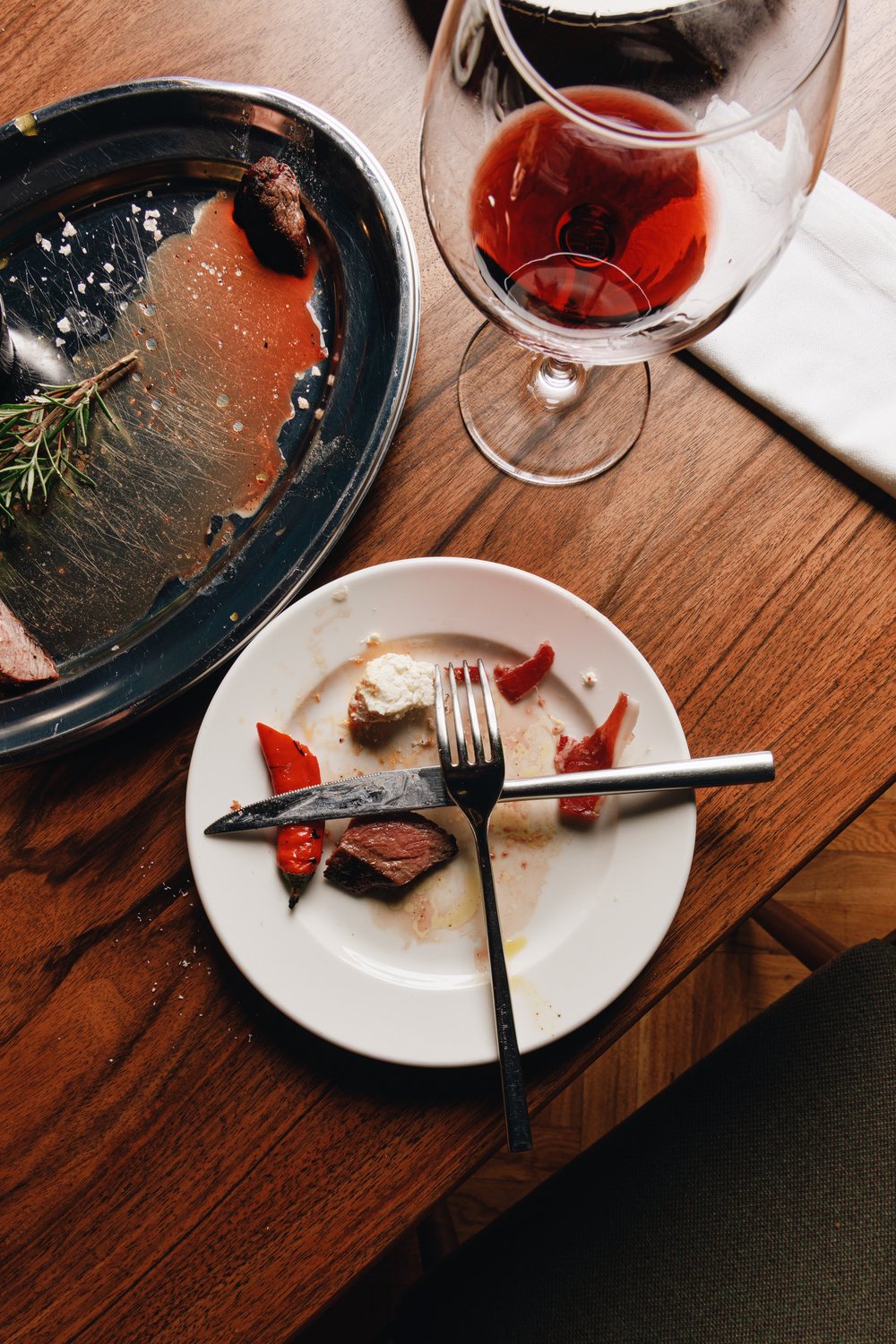 Finished steak, a cleared platter and a glass of red wine on a walnut table
