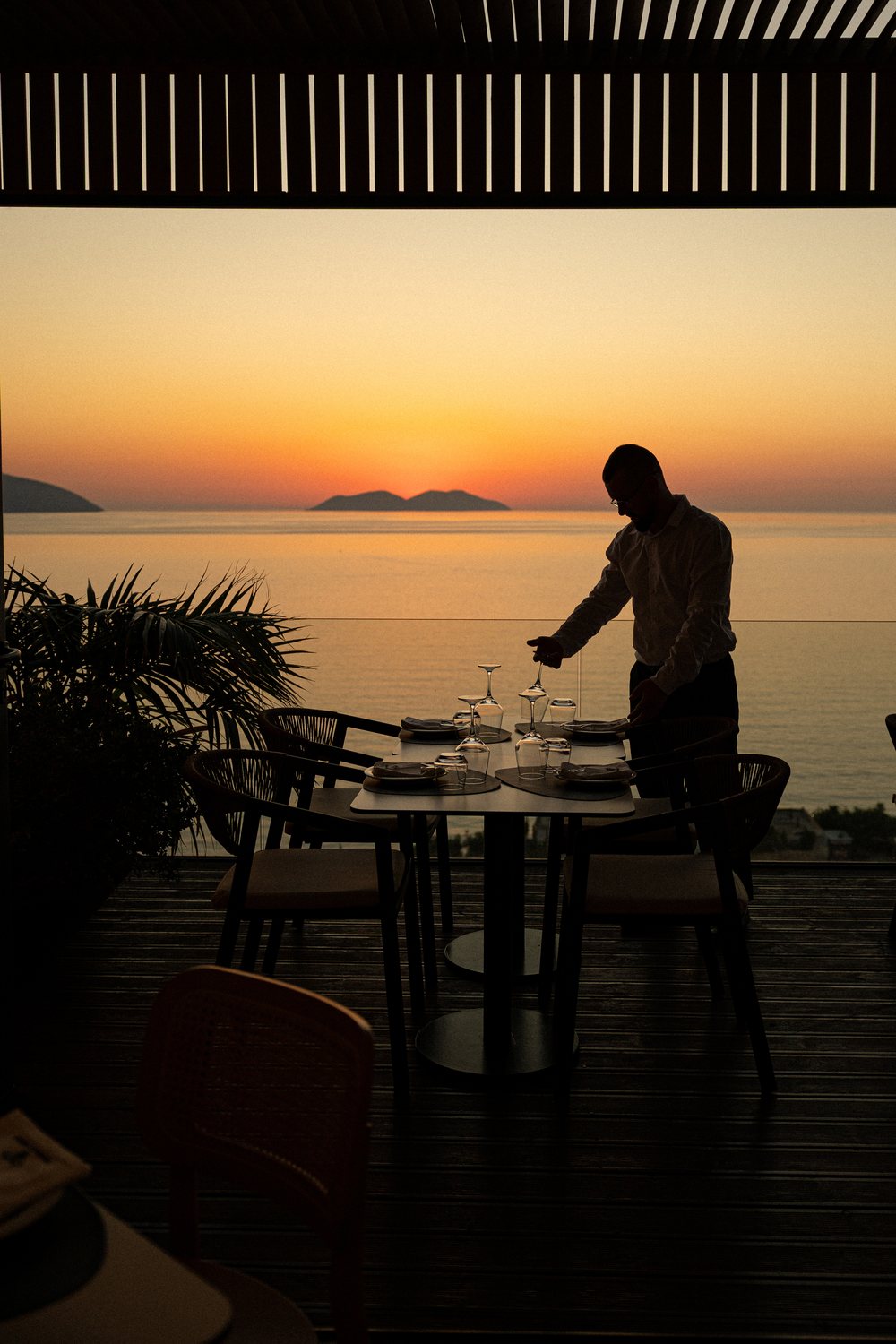 Waiter setting a table on the terrace at sunset over the islands