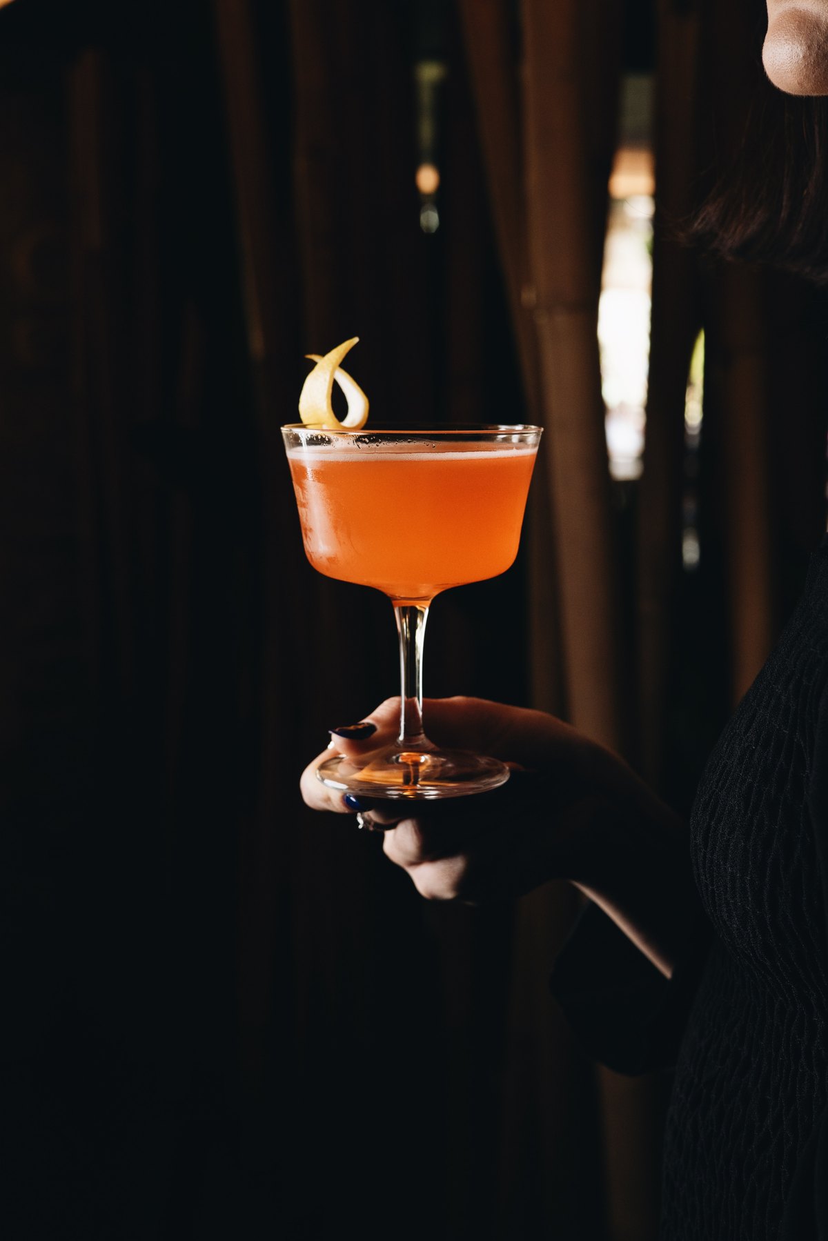 Hand holding a coupe cocktail with a lemon twist