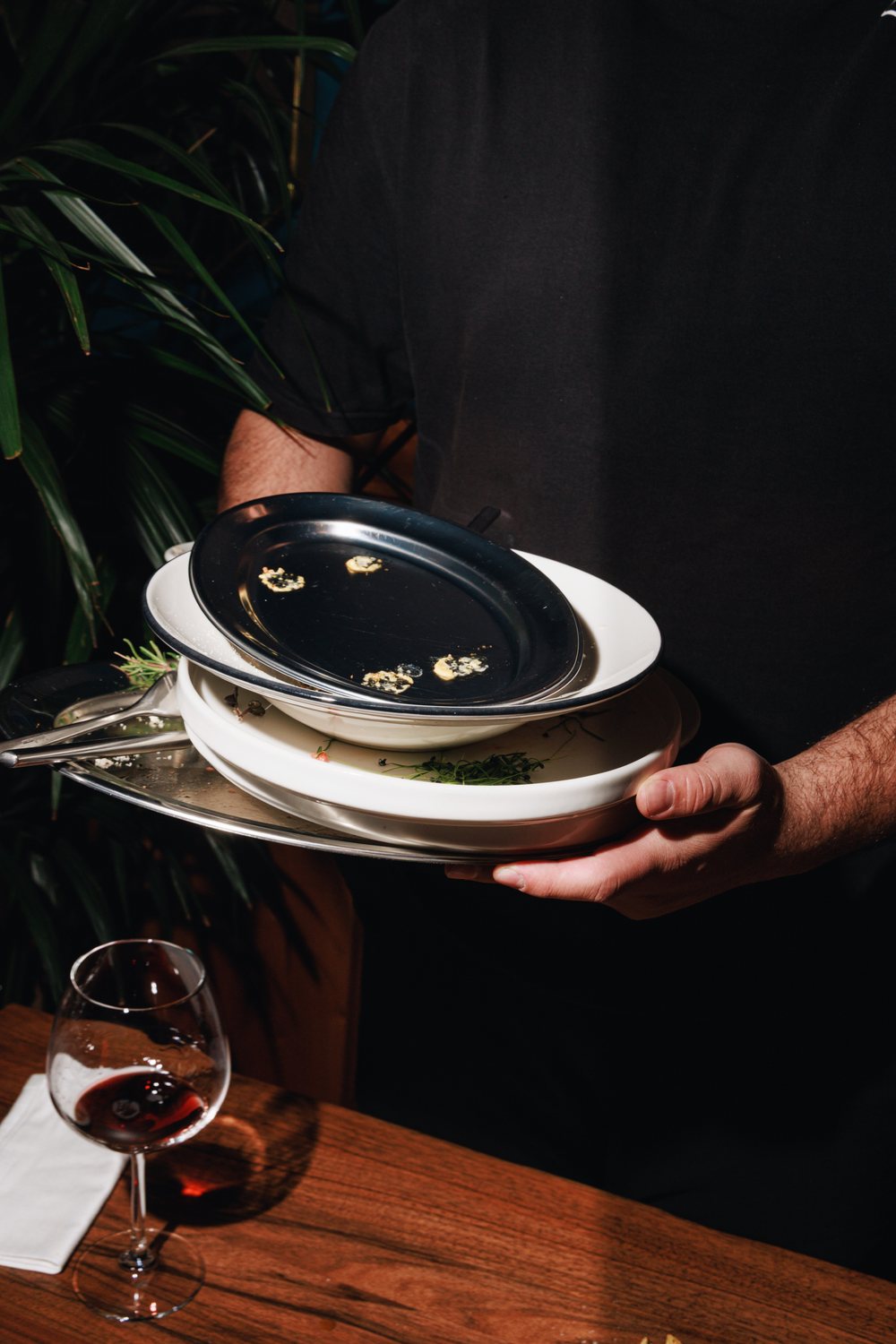 Waiter clearing a stack of empty plates beside a glass of red wine