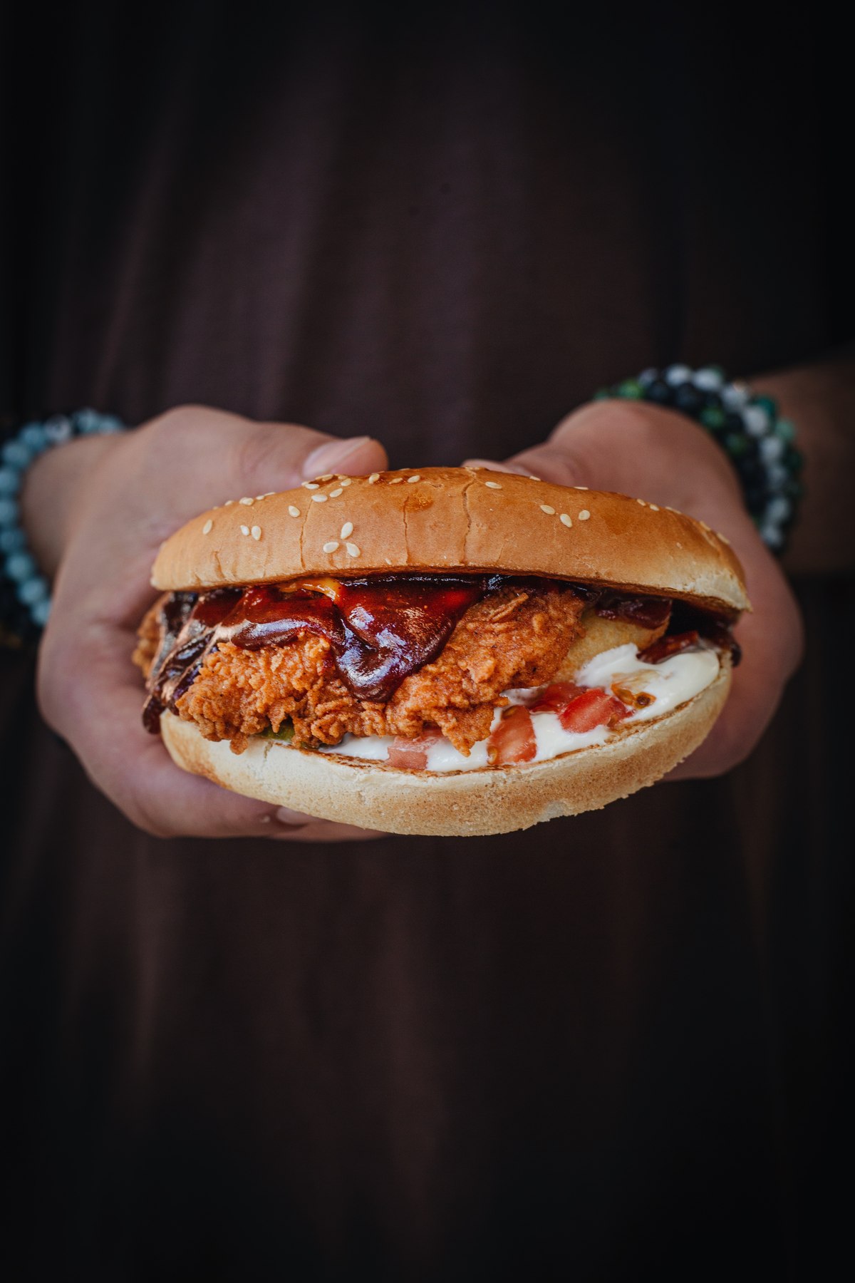 Hands holding a crispy chicken burger with barbecue sauce