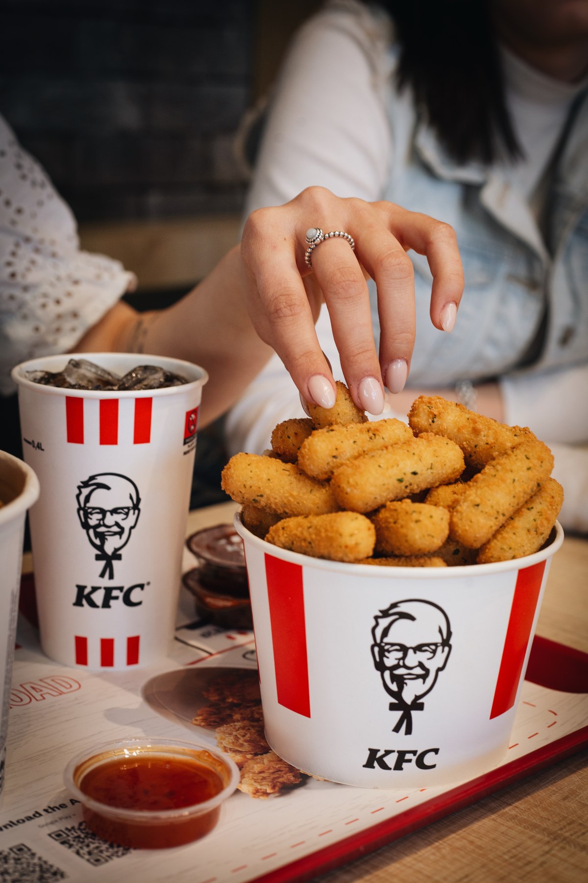 Hand reaching into a KFC bucket of mozzarella sticks beside a drink