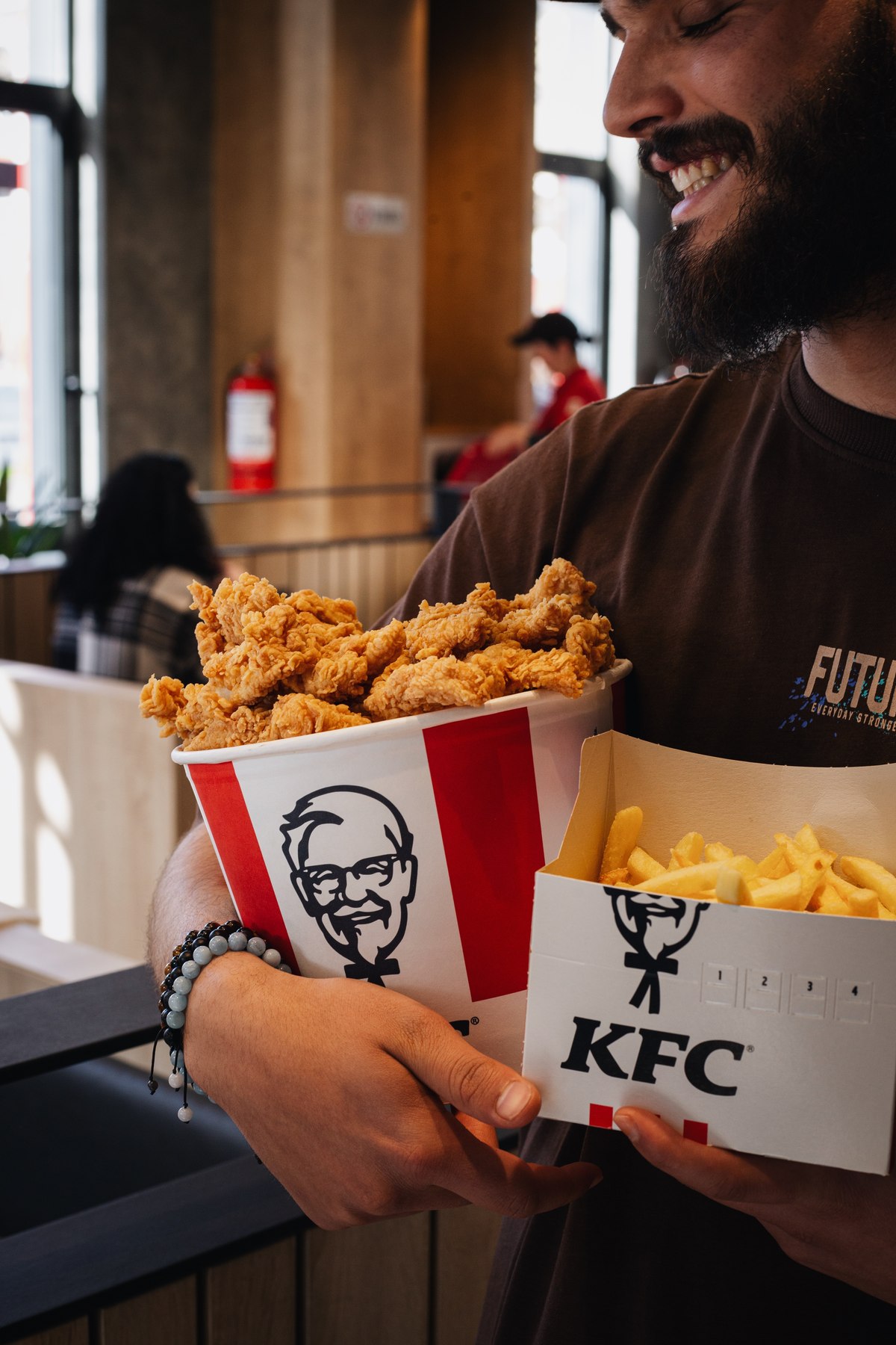Smiling man hugging a KFC bucket of crispy strips and a box of fries in the restaurant