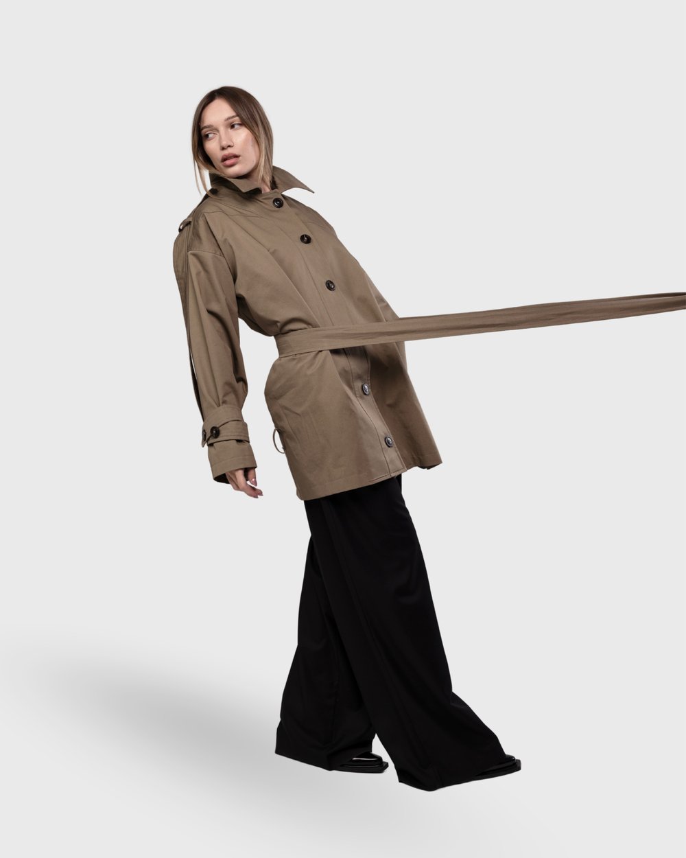 Model in a khaki trench with the belt flying across the frame