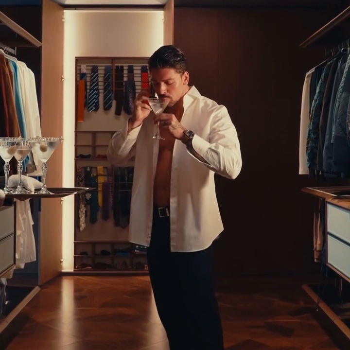Man in an open white shirt sipping a martini in a dressing room, from the LE BAR campaign