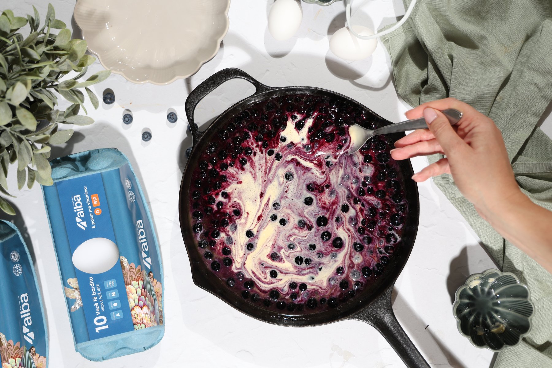Blueberry batter swirled in a cast iron skillet beside AIBA cartons