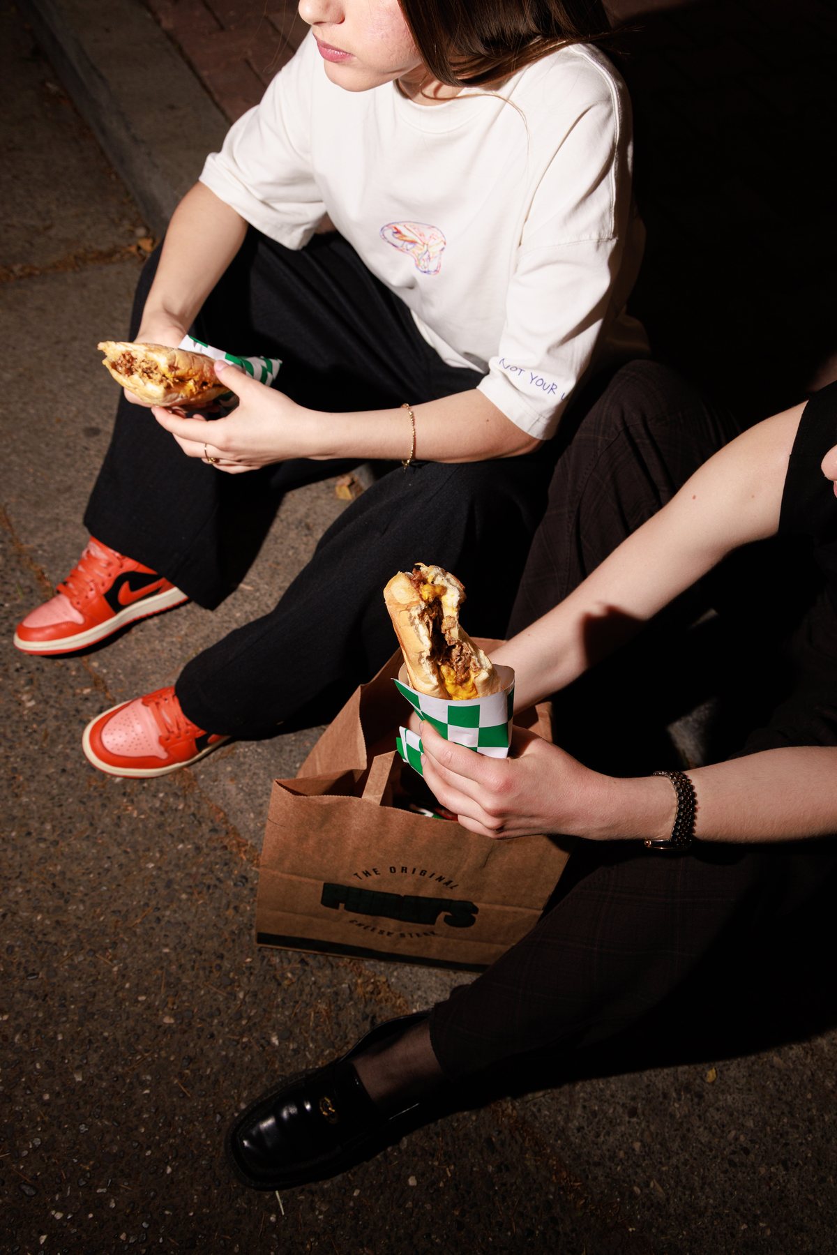 Two friends eating cheesesteaks on the curb