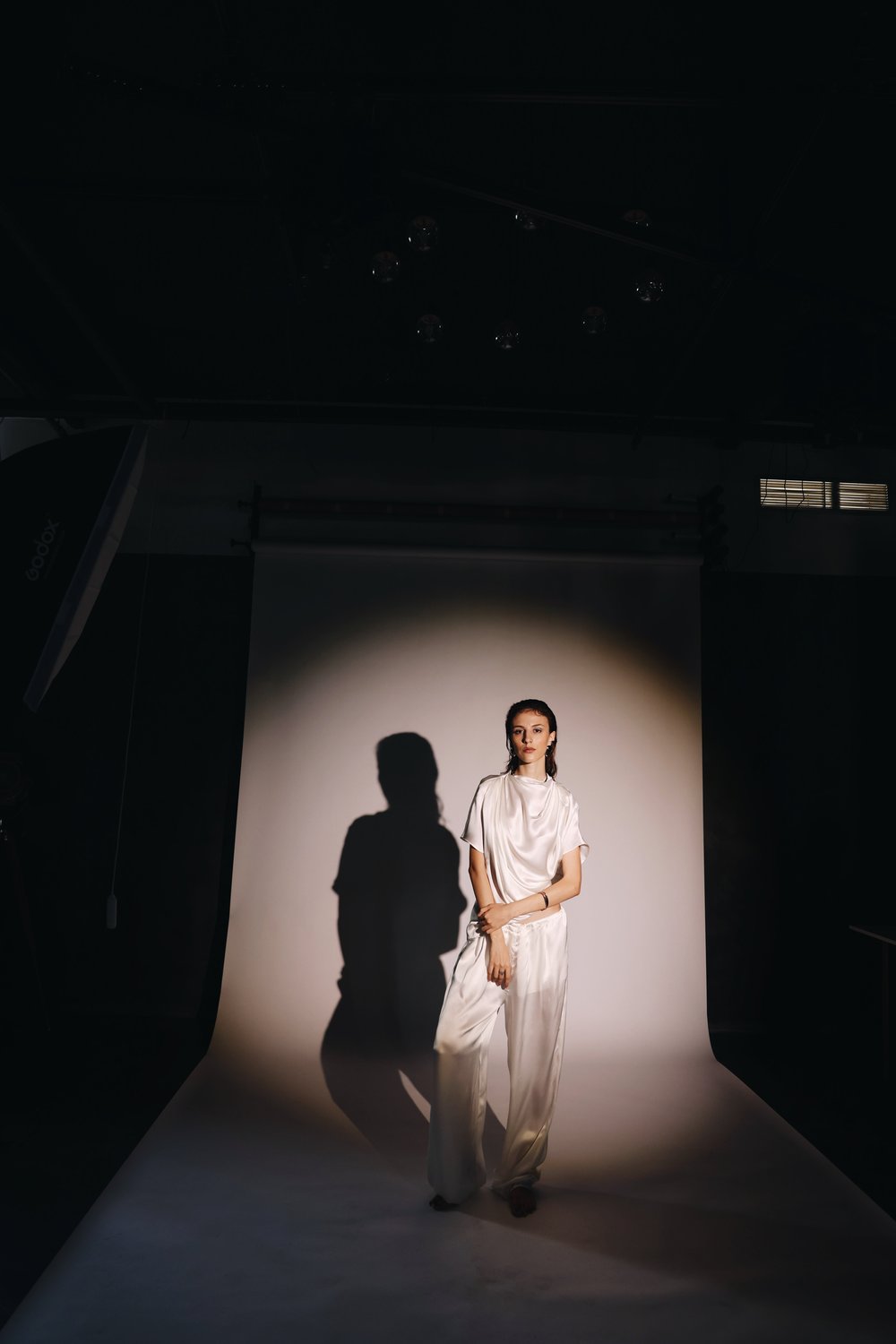 Model in white satin standing in a spotlight on a studio backdrop