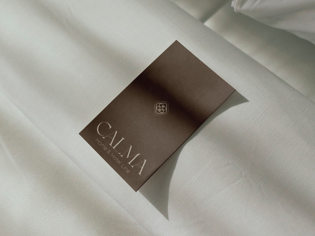 Brown Calma Home & Hotel Line label card on white linen