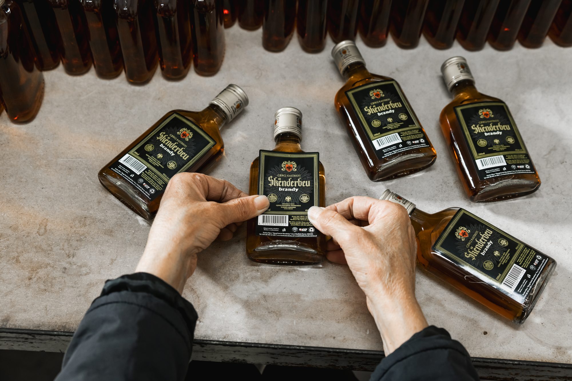Hands applying labels to Skënderbeu brandy flasks