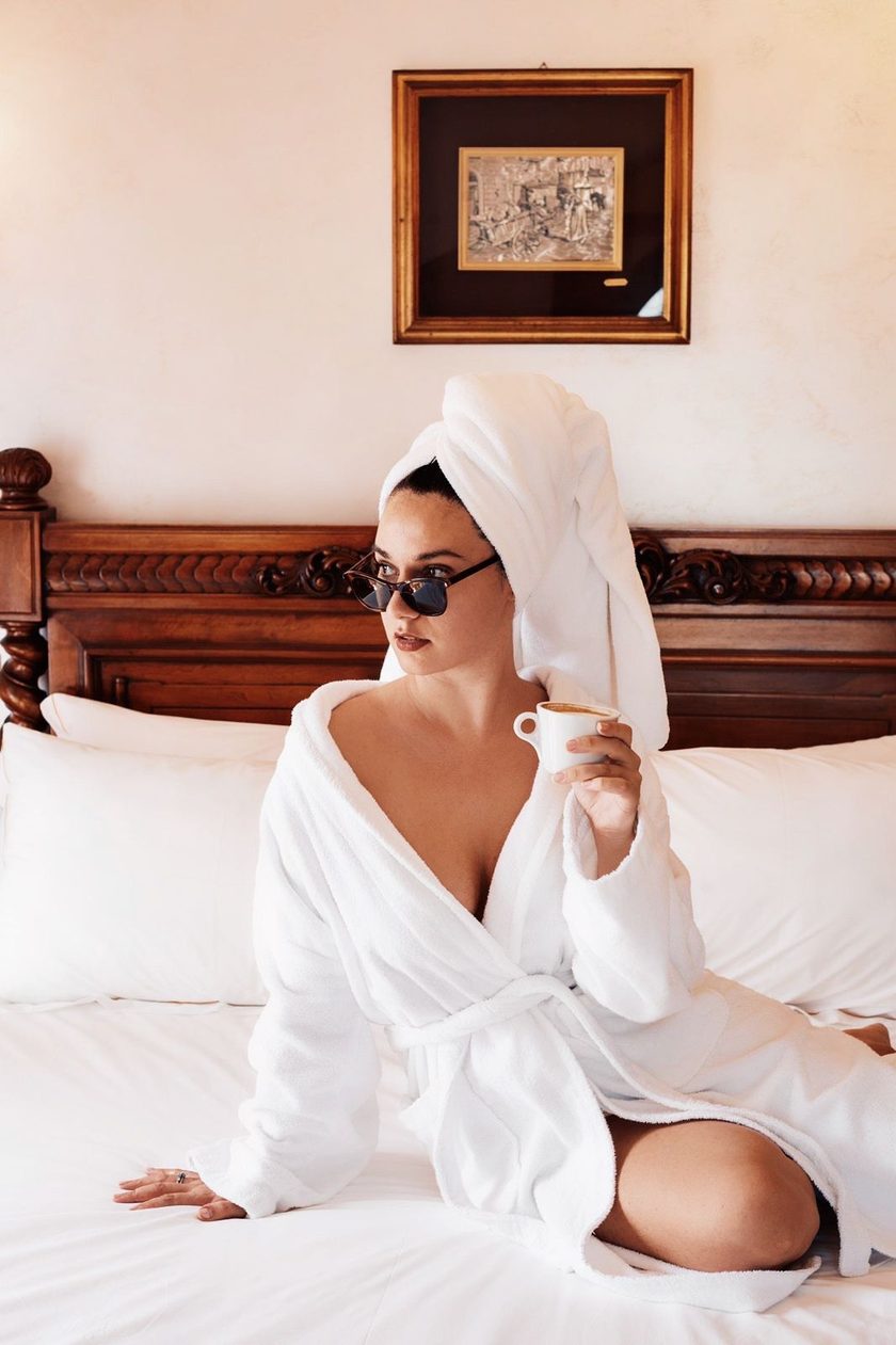Guest in a robe and sunglasses sipping coffee in bed