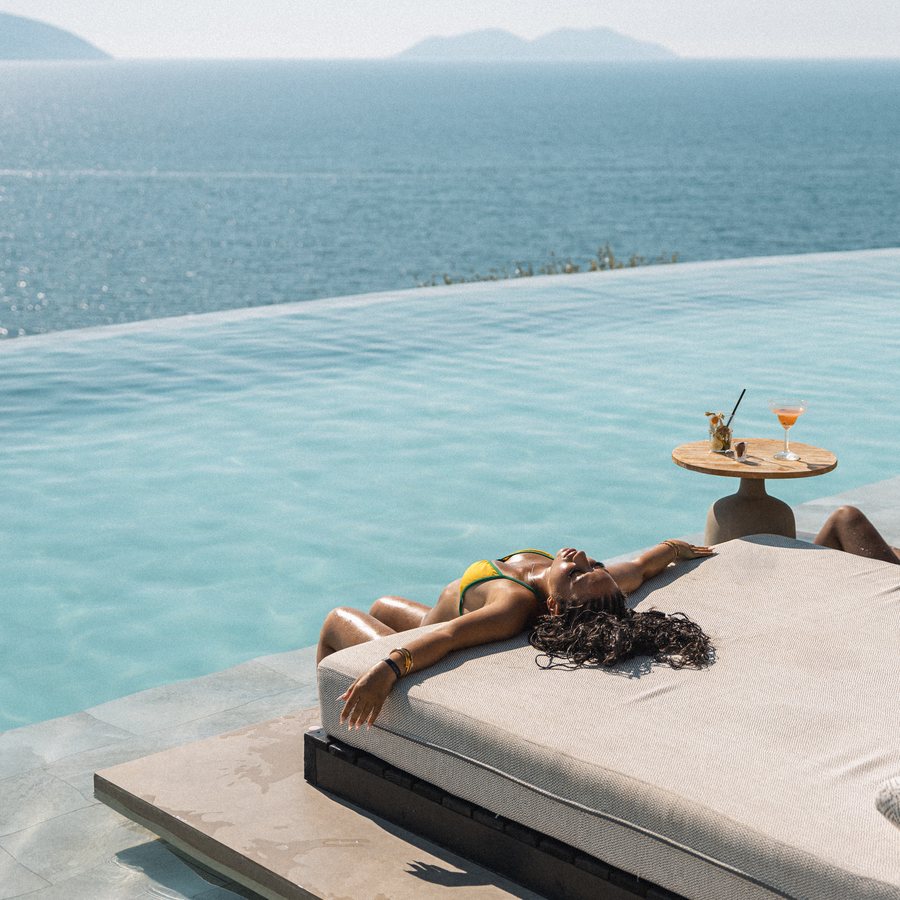 Guest sunbathing on a daybed by the Nobus infinity pool above the sea