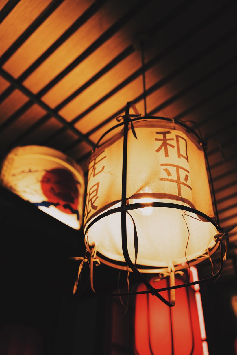 Paper lantern with Japanese characters glowing under a wooden ceiling