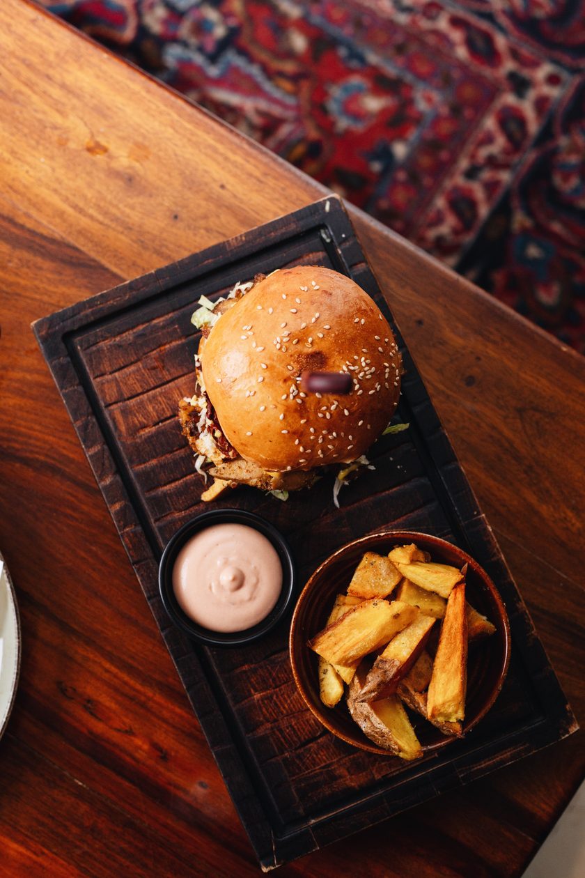 Burger and potato wedges on a board over a Persian rug