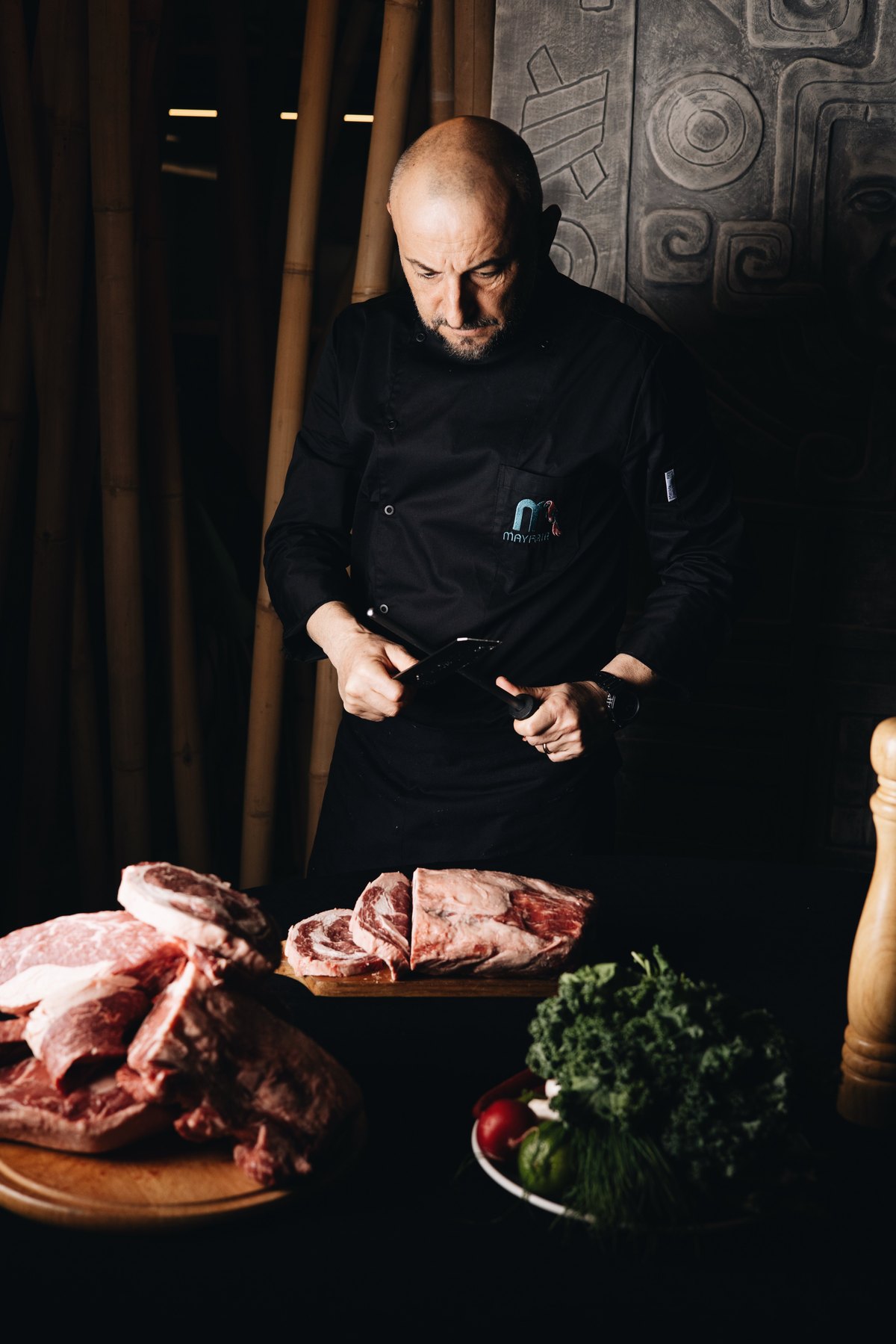 Mayfair chef sharpening a knife behind cuts of raw beef