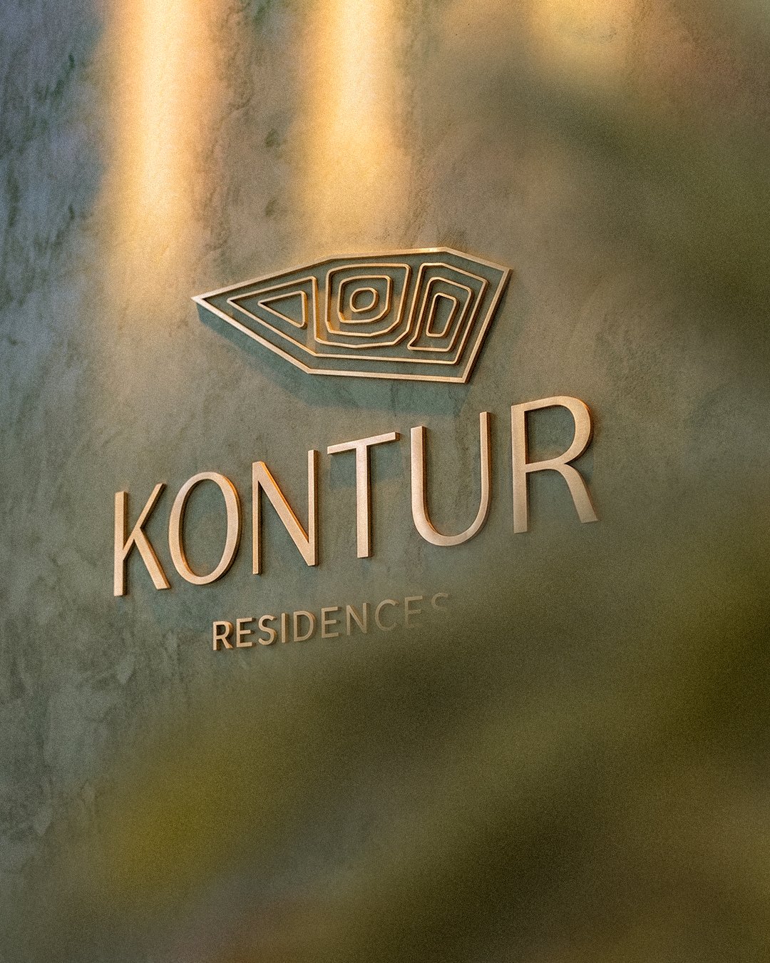 Brass Kontur Residences sign on a green plaster wall in warm light