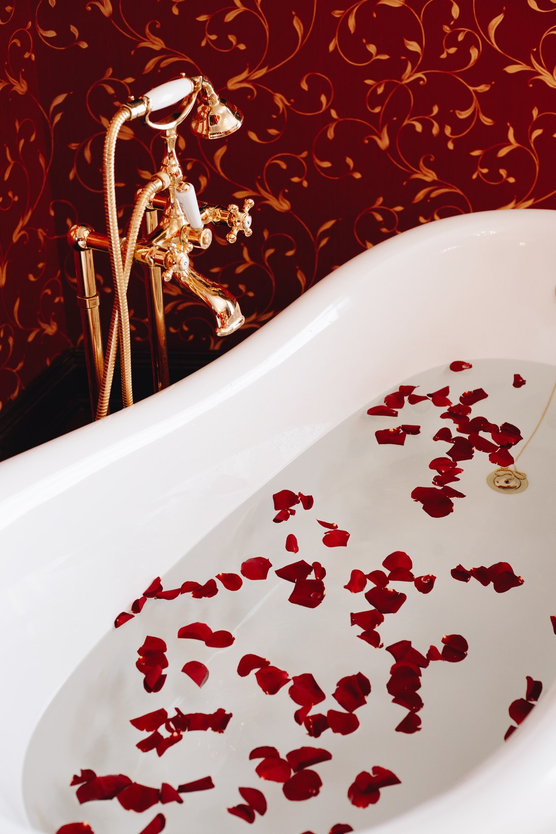 Rose petals floating in a clawfoot bath with gold taps