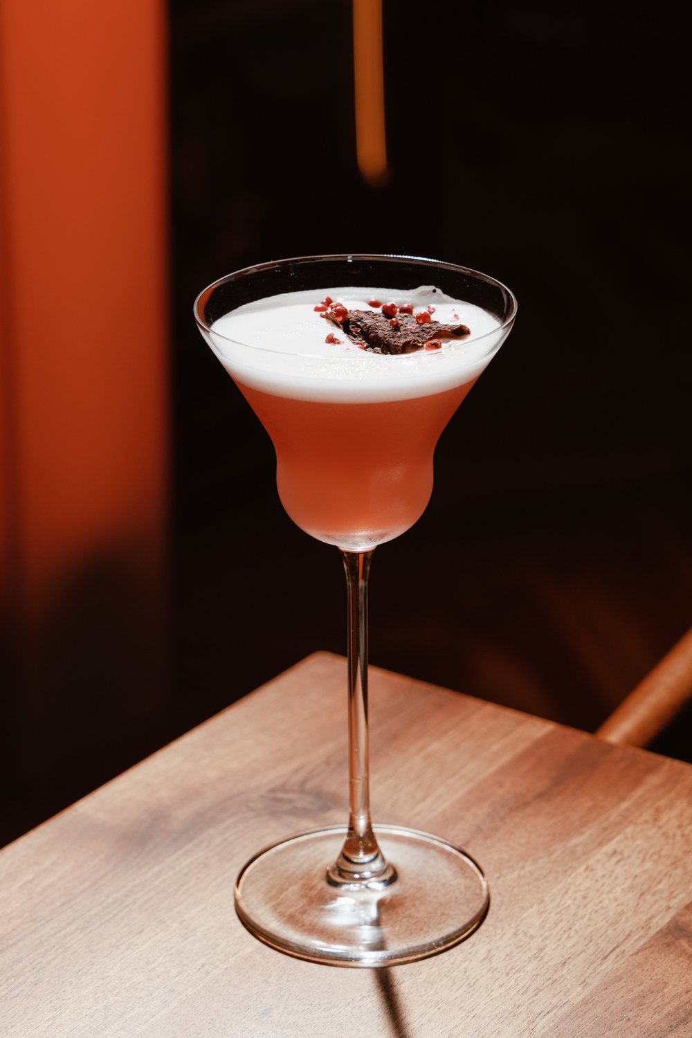 Cocktail with foam, pink peppercorns and a crisp, in warm orange light