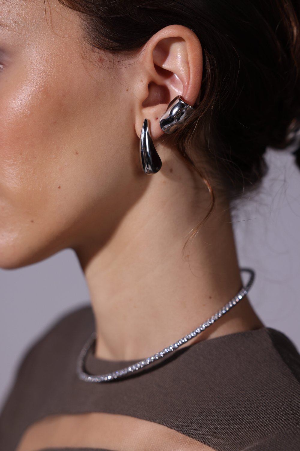 Close-up of silver teardrop earring, ear cuff and crystal choker