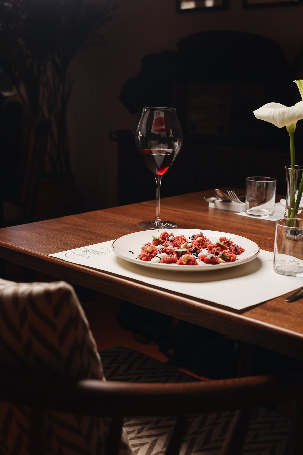 Beef tartare with a glass of red wine and a calla lily