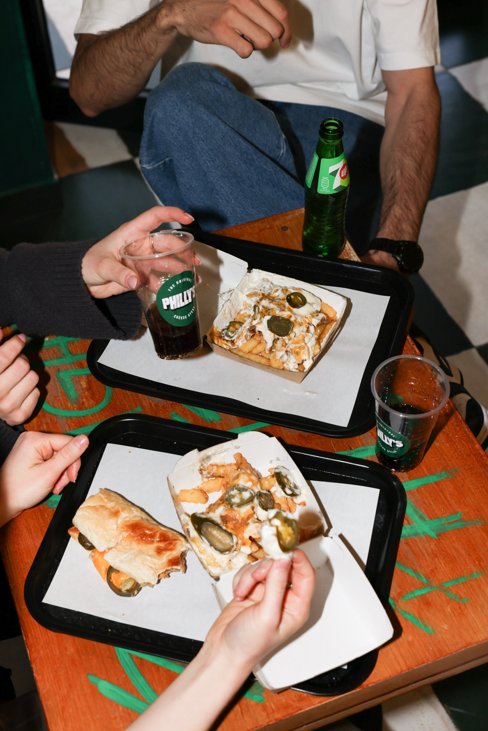Friends sharing cheesesteaks and loaded fries on trays at Philly&rsquo;s